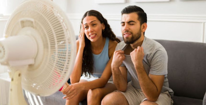 A couple in front of a standing fan trying to beat the heat
